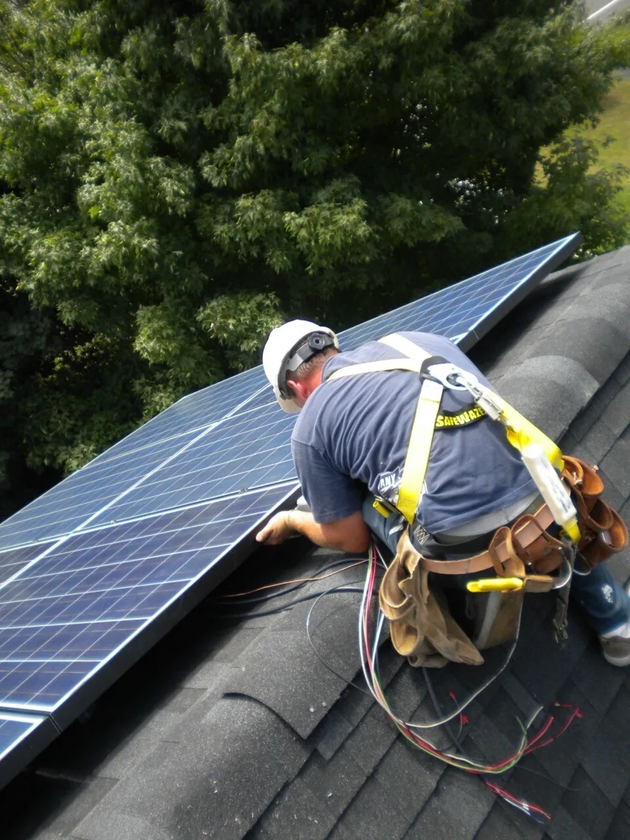 Installer in a harness wiring a solar array on a shingle roof