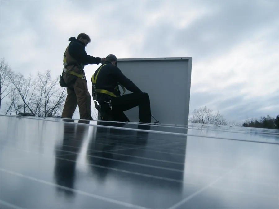 Two Sun Directed installers in harnesses setting a solar module on a roof
