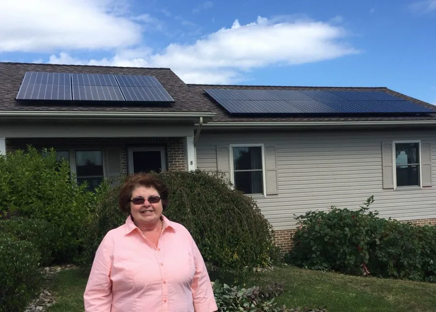 Sun Directed customer smiling in front of her home's rooftop solar array