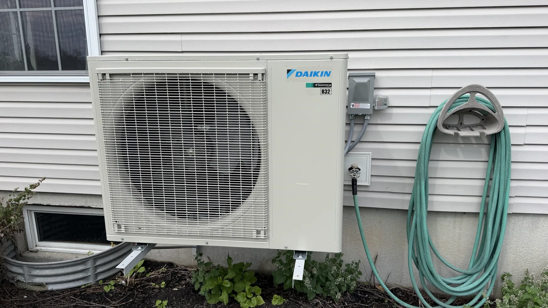 Daikin inverter heat pump outdoor unit installed on the side of a home, beside its service disconnect