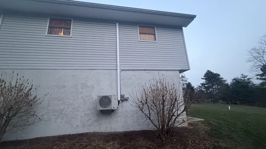 Compact outdoor unit near the foundation with line-set covers running up the wall