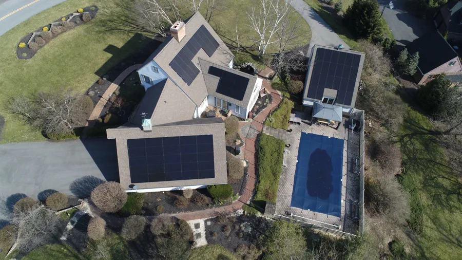 Aerial view of a home with solar arrays on the main roof, garage, and pool house