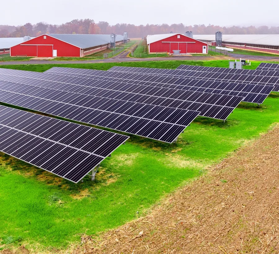 Ground-mount solar array in a field in front of red agricultural barns
