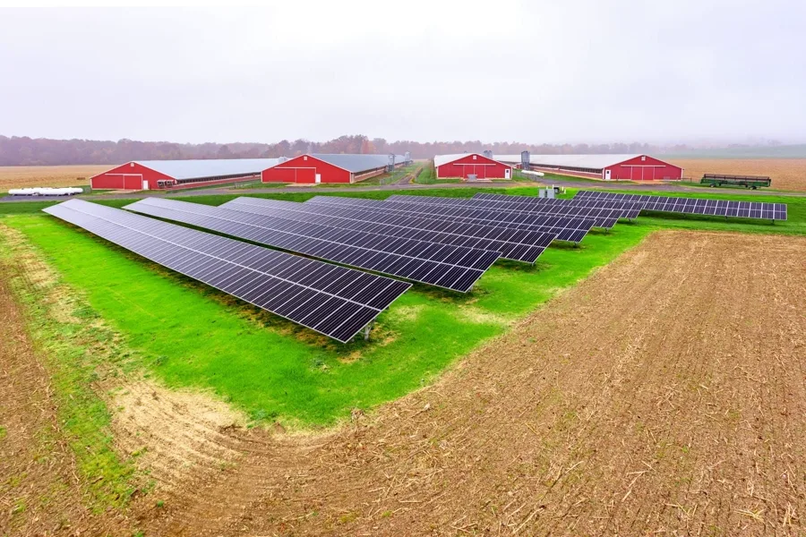 Ground-mount solar array in a field in front of red agricultural barns.